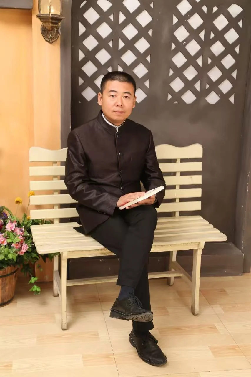 宋岩松身穿中式服装，手持书本坐于长椅